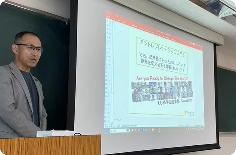 教室で登壇者が講義を行い、スクリーンに『アントレプレナーシップ入門』のスライドが投影されている様子