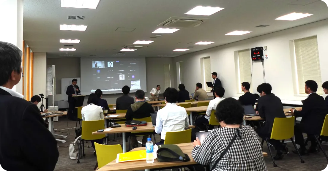 ビジネスプランコンテストの発表会場で、参加者が着席しスクリーンを見ながらプレゼンテーションを聞いている様子